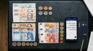 Banknotes and coins of Czech Koruna, Hungarian Forint, and Euro arranged on a slate table with smartphone currency converter (AI Generated Image)